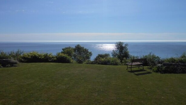A grassy lawn with a bench and a view of the ocean.