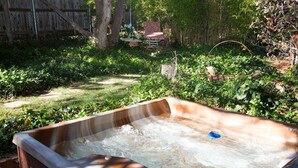 A hot tub in a garden with a wooden fence and trees in the background.