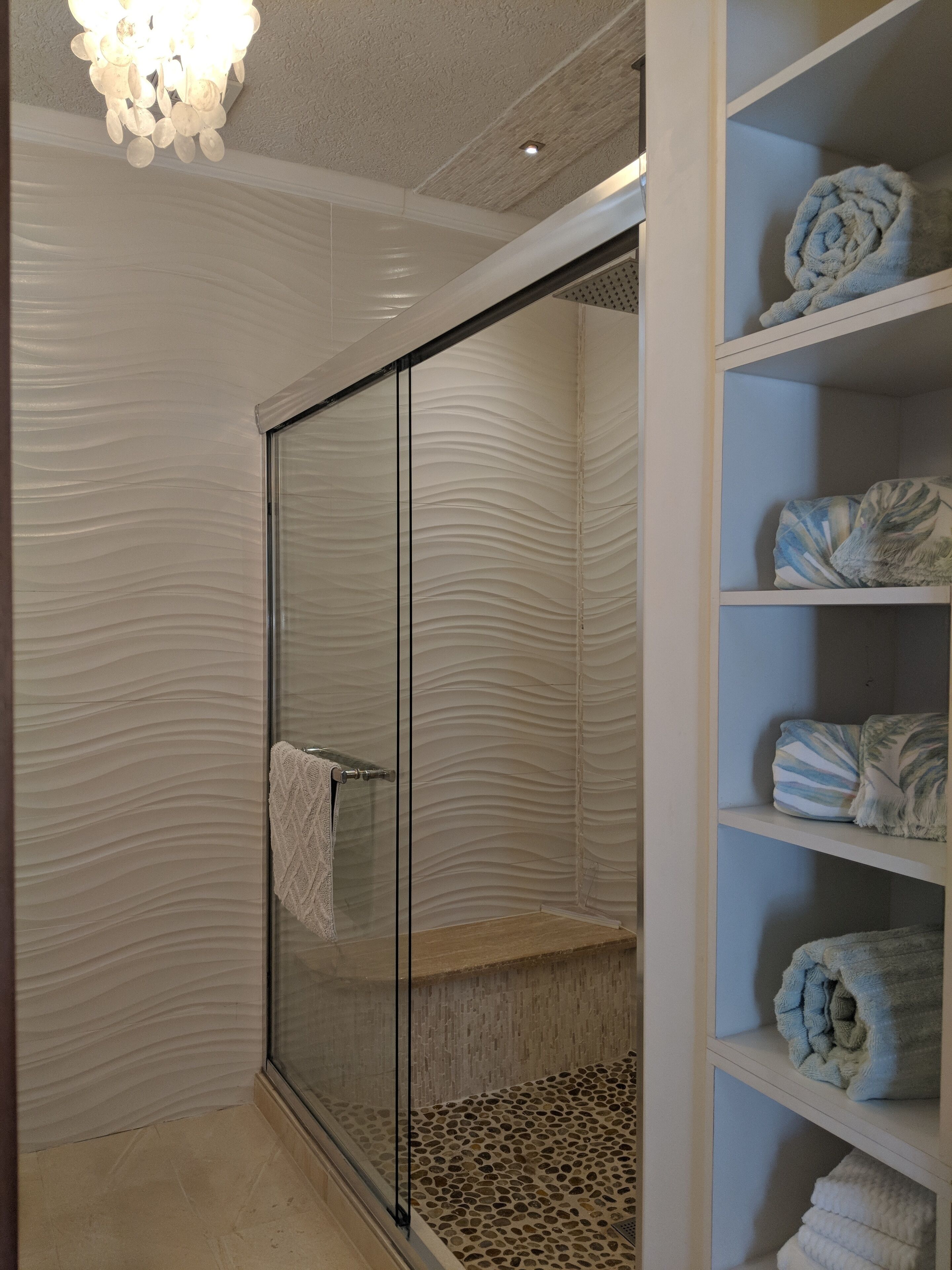 Ein modernes Badezimmer mit Duschkabine aus Glas, einer strukturierten Wand und einem Ablagebereich mit ordentlich gefalteten Handtüchern.