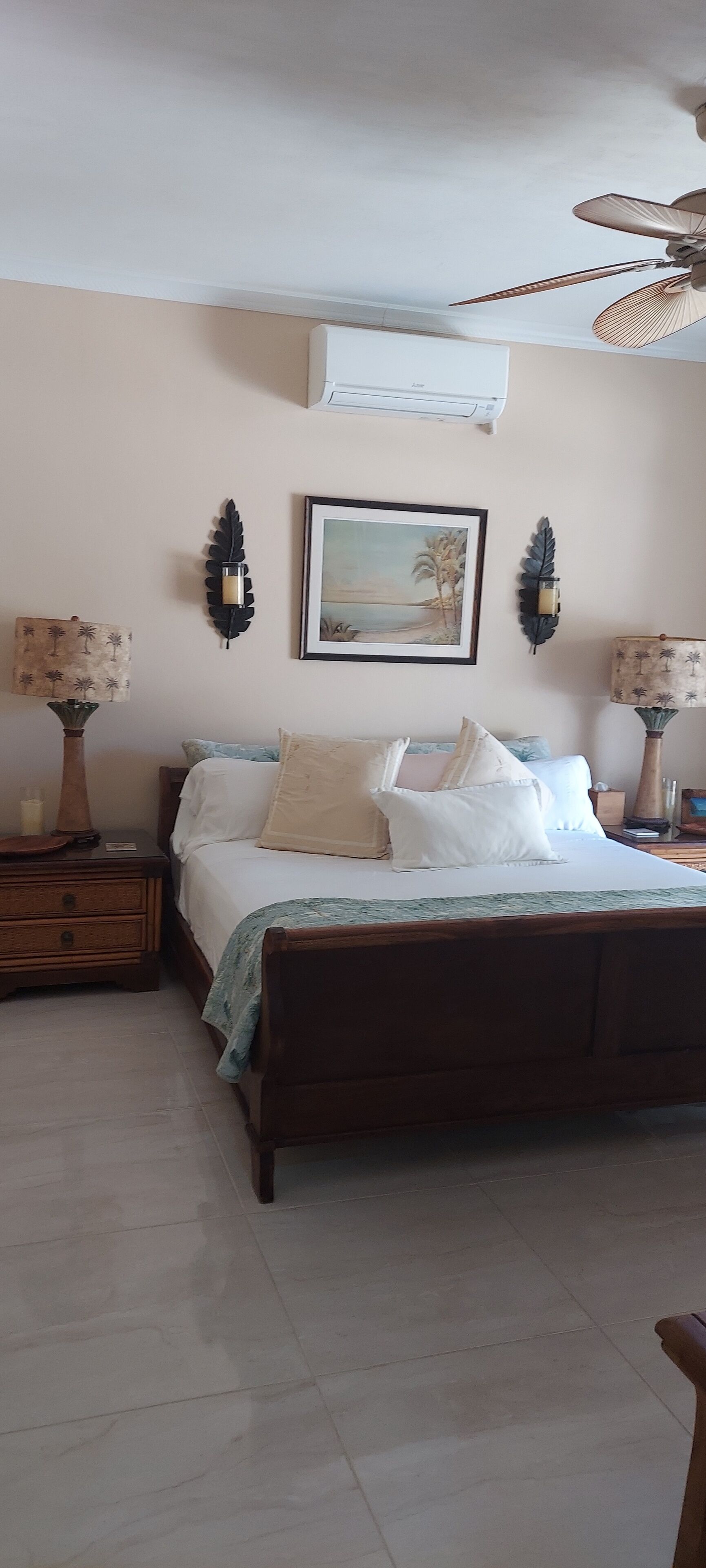 Een slaapkamer met een houten bed, twee wandlampen, een plafondventilator en een ingelijste foto aan de muur.