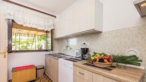 A compact kitchen with a window, a coffee maker, and a fruit basket on the counter.
