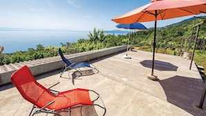 An outdoor terrace with two chairs and an umbrella, overlooking a scenic landscape with a body of water and hills.