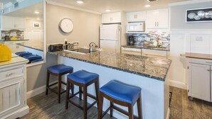 A modern kitchen with a granite countertop, white cabinets, and a clock on the wall. - STUNNING GULF FRONT VIEW! (Destin)
