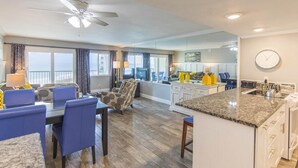 A modern kitchen with a granite countertop, a dining area with blue chairs, and a large island. - STUNNING GULF FRONT VIEW! (Destin)