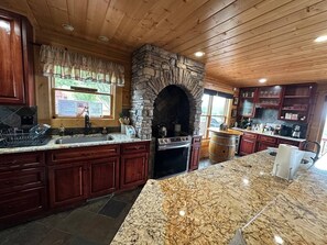 A kitchen with a stone fireplace, granite countertops, and wooden cabinetry.