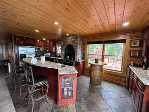 Une cuisine avec une cheminée en pierre, un plafond en bois et une grande fenêtre.
