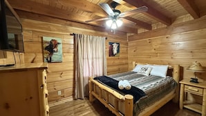 Ein Schlafzimmer einer Holzhütte mit einem Bett, einem Nachttisch, einem Deckenventilator und einem Fenster.