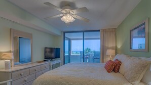 Habitación de hotel con cama, televisor, cómoda y balcón con vistas.