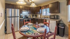 Una cocina con un refrigerador de acero inoxidable, un microondas y una mesa de comedor preparada para cuatro.
