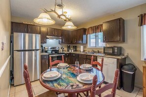 Una cocina con un refrigerador de acero inoxidable, un microondas y una mesa de comedor preparada para cuatro.