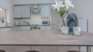 A modern kitchen with white cabinets, a microwave, and a coffee machine. There is a vase with white flowers on the counter. - Eden Lodge (High Wycombe)