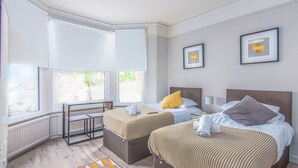 A hotel room with two beds, a small table, and a bench. - Eden Lodge (High Wycombe)