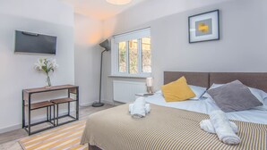 A modern hotel room with a bed, bedside table, TV, and a window with a view. - Eden Lodge (High Wycombe)
