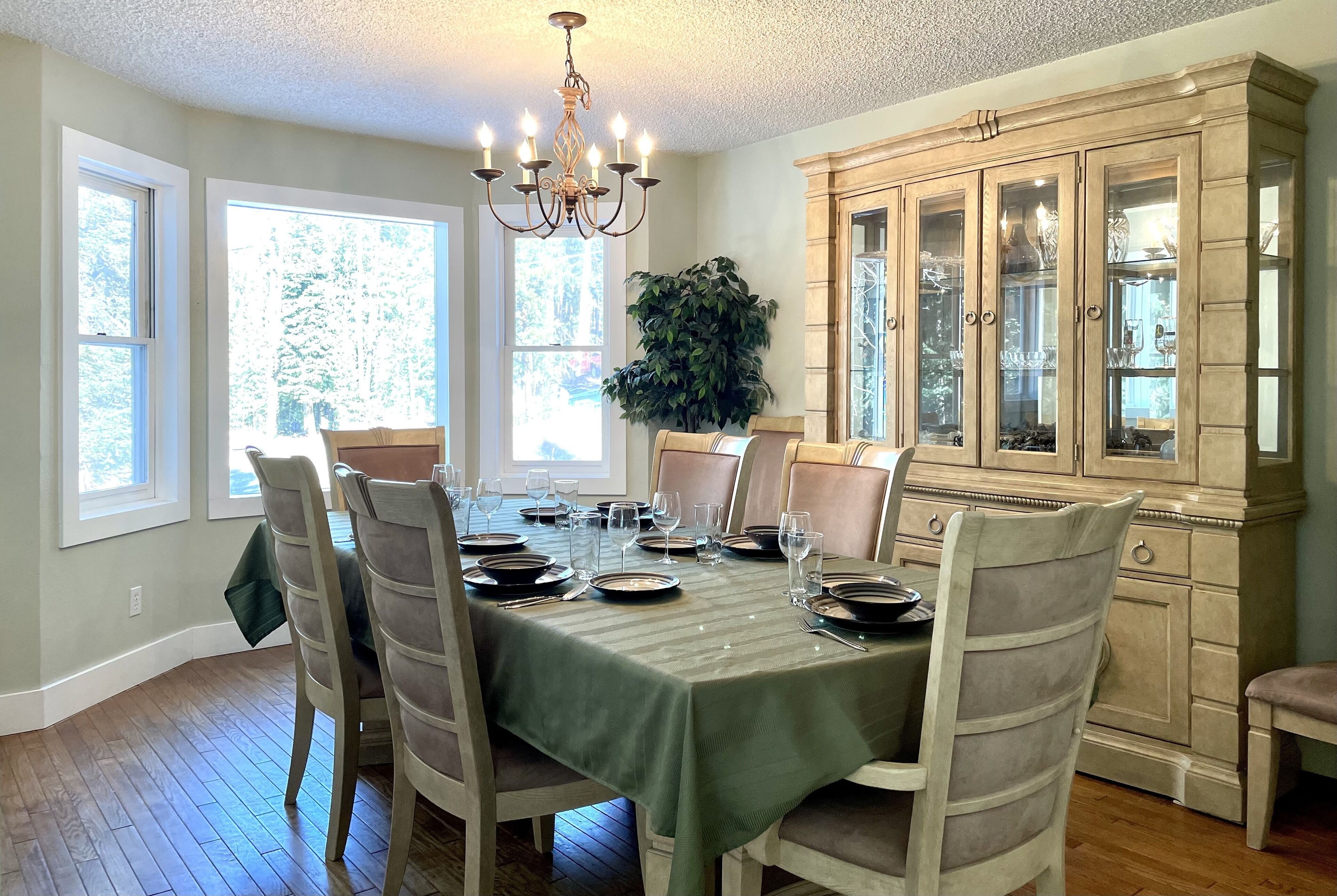 A dining room with a green tablecloth, wooden chairs, a chandelier, and a cabinet with glass doors.