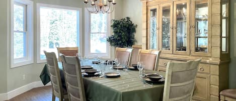 A dining room with a green tablecloth, wooden chairs, a chandelier, and a cabinet with glass doors.