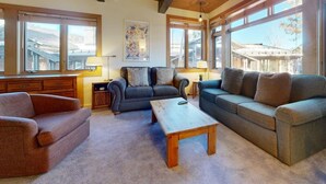 Ein geräumiges Wohnzimmer mit Holzbalkendecke, großen Fenstern, einer Sofagarnitur, einem Couchtisch und einer Lampe.