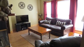 A living room with a leather sofa, a wooden coffee table, a flat-screen TV, and decorative wall art.