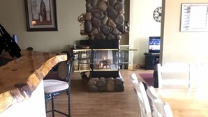 A cozy living area with a stone fireplace, wooden flooring, and a dining table with chairs.
