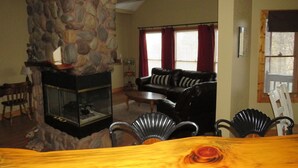 A living room with a stone fireplace, a black leather sofa, and a dining area with a wooden table and chairs.