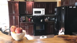 A kitchen with dark wooden cabinets, a white microwave, a black refrigerator, and a wooden island with a bowl of fruit.