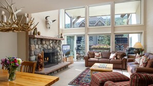 A spacious living room with a stone fireplace, leather sofas, and a large window overlooking a scenic landscape. - Montaneros 408 - 3 Bedroom Platinum (Vail)