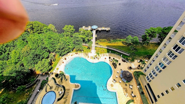 Un hotel moderno de gran altura con una amplia piscina, un muelle que se adentra en una gran extensión de agua, y exuberante vegetación alrededor de la propiedad.