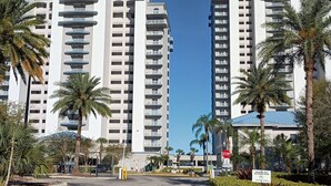 Un edificio residencial alto con varios balcones, rodeado de palmeras y un cielo azul despejado.