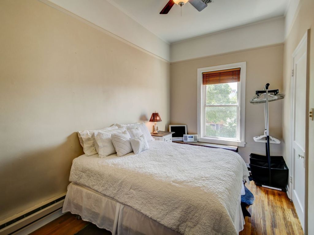 A bedroom with a large bed, a window with blinds, a heater, a lamp, and a floor lamp.