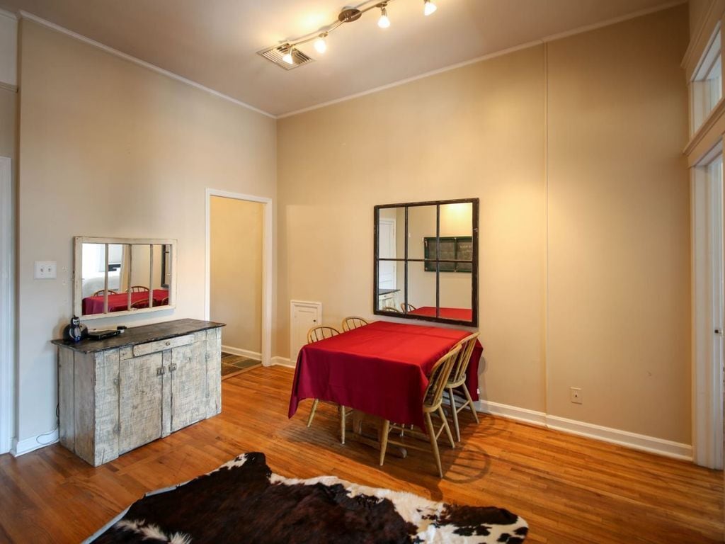 A room with a wooden floor, a dining table with a red tablecloth, a mirror on the wall, and a cowhide rug.