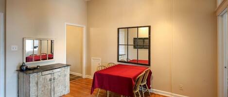 A room with a wooden floor, a dining table with a red tablecloth, a mirror on the wall, and a cowhide rug.