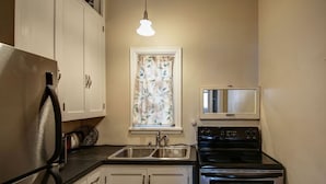 A compact kitchen with white cabinets, a stainless steel refrigerator, a double oven, and a microwave. - Downtown Bozeman Apartment Above Main Street, Monthly + Extended Stays (Bozeman)