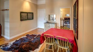 A room with a dining table, chairs, a red tablecloth, a cowhide rug, a framed picture, a mirror, and a kitchen area in the background. - Downtown Bozeman Apartment Above Main Street, Monthly + Extended Stays (Bozeman)