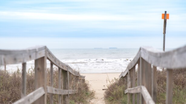 A wooden boardwalk leading to a beach with a sandy shore and the ocean in the background. - Beautiful newer beach house with spectacular ocean views and right at the beach! (Surfside Beach)