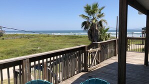 A wooden deck with two blue Adirondack chairs facing a beach with ocean waves and a palm tree. - Beautiful newer beach house with spectacular ocean views and right at the beach! (Surfside Beach)