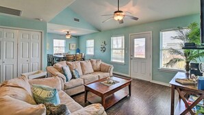 A spacious living room with a large sectional sofa, a coffee table, and a ceiling fan. There are two doors and windows with blinds. - Beautiful newer beach house with spectacular ocean views and right at the beach! (Surfside Beach)