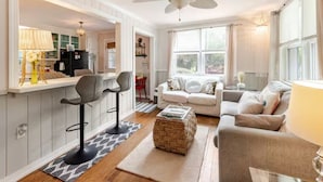 A modern living room with a sofa, two bar stools, a coffee table, and a ceiling fan. - PERFECT LOCATION 3 Blocks to Sand, Sun, and Folly Fun "Park car and Forget It!" (Folly Beach)