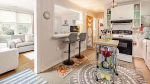 A modern kitchen with white cabinets, a stove, and a dining area with two chairs. - PERFECT LOCATION 3 Blocks to Sand, Sun, and Folly Fun "Park car and Forget It!" (Folly Beach)
