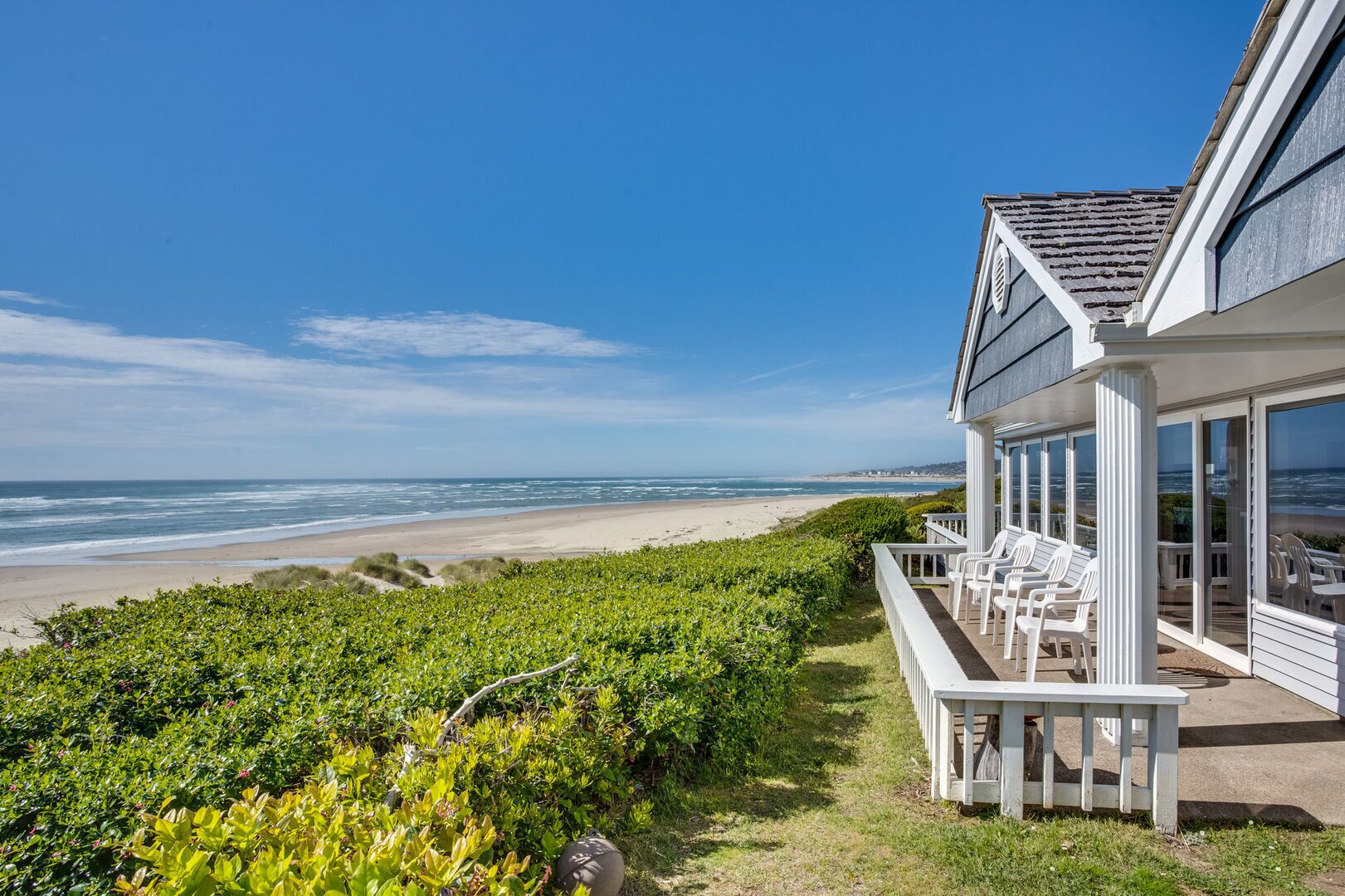 A beachfront property with a patio overlooking the ocean, a garden area, and a building with large windows.