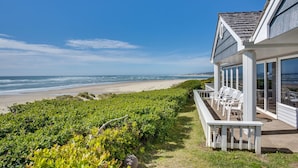 A beachfront property with a patio overlooking the ocean, a garden area, and a building with large windows. - Beach Front Panoramic Vistas! Miles of Sandy Beach! Hot Tub! Dog Friendly! (Waldport)