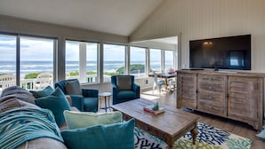 A spacious living room with a large TV, comfortable seating, and a view of the ocean. - Beach Front Panoramic Vistas! Miles of Sandy Beach! Hot Tub! Dog Friendly! (Waldport)