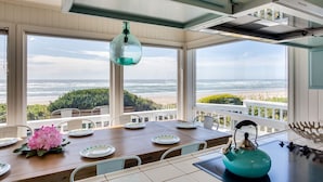A dining area with a view of the ocean, a hanging light fixture, and a kitchen area with a kettle. - Beach Front Panoramic Vistas! Miles of Sandy Beach! Hot Tub! Dog Friendly! (Waldport)
