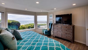 A bedroom with a large bed, a dresser, a TV, and a view of the ocean. - Beach Front Panoramic Vistas! Miles of Sandy Beach! Hot Tub! Dog Friendly! (Waldport)