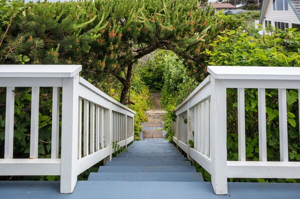 A staircase with white railings leading up to a tree archway surrounded by greenery.