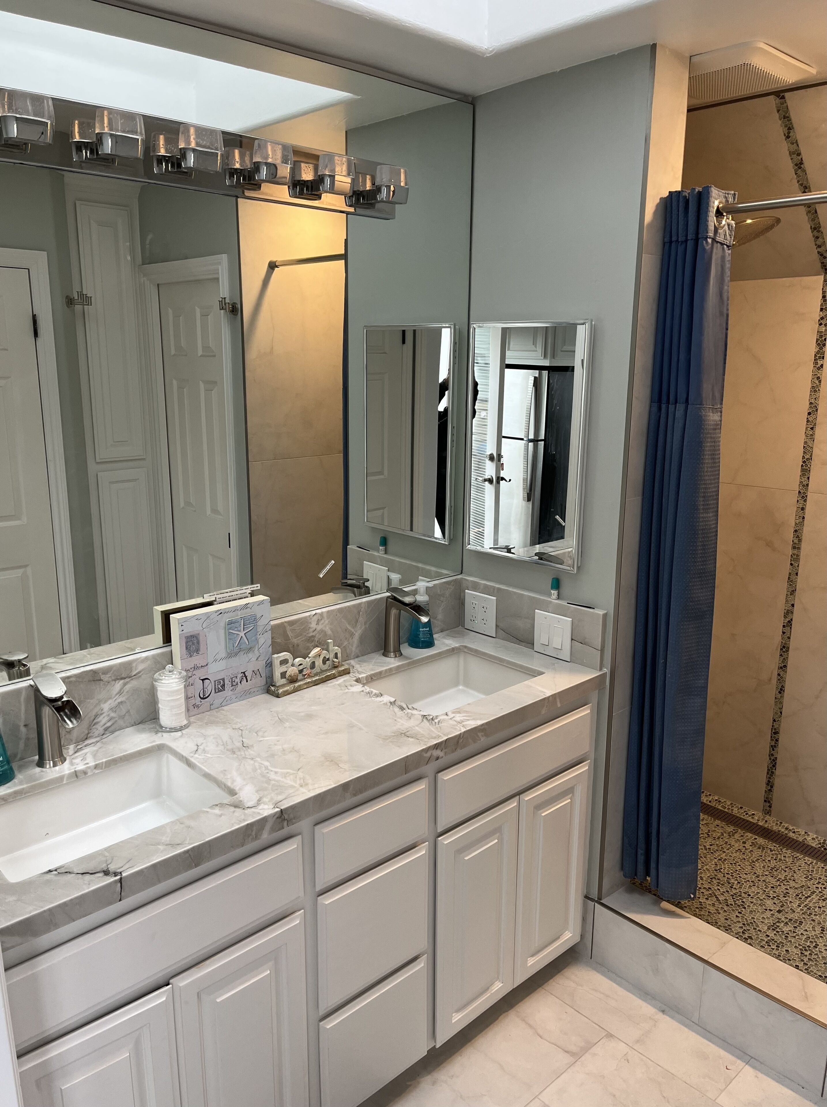 A modern bathroom with a large mirror, two sinks, and a shower area.