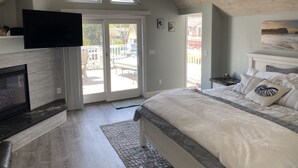 A bedroom with a large bed, a fireplace, a TV mounted on the wall, and a view through the door. - Clean, Newly Remodeled Home Steps to  Beach, HOT TUB, LARGE deck  w/ocean peek (Santa Cruz)