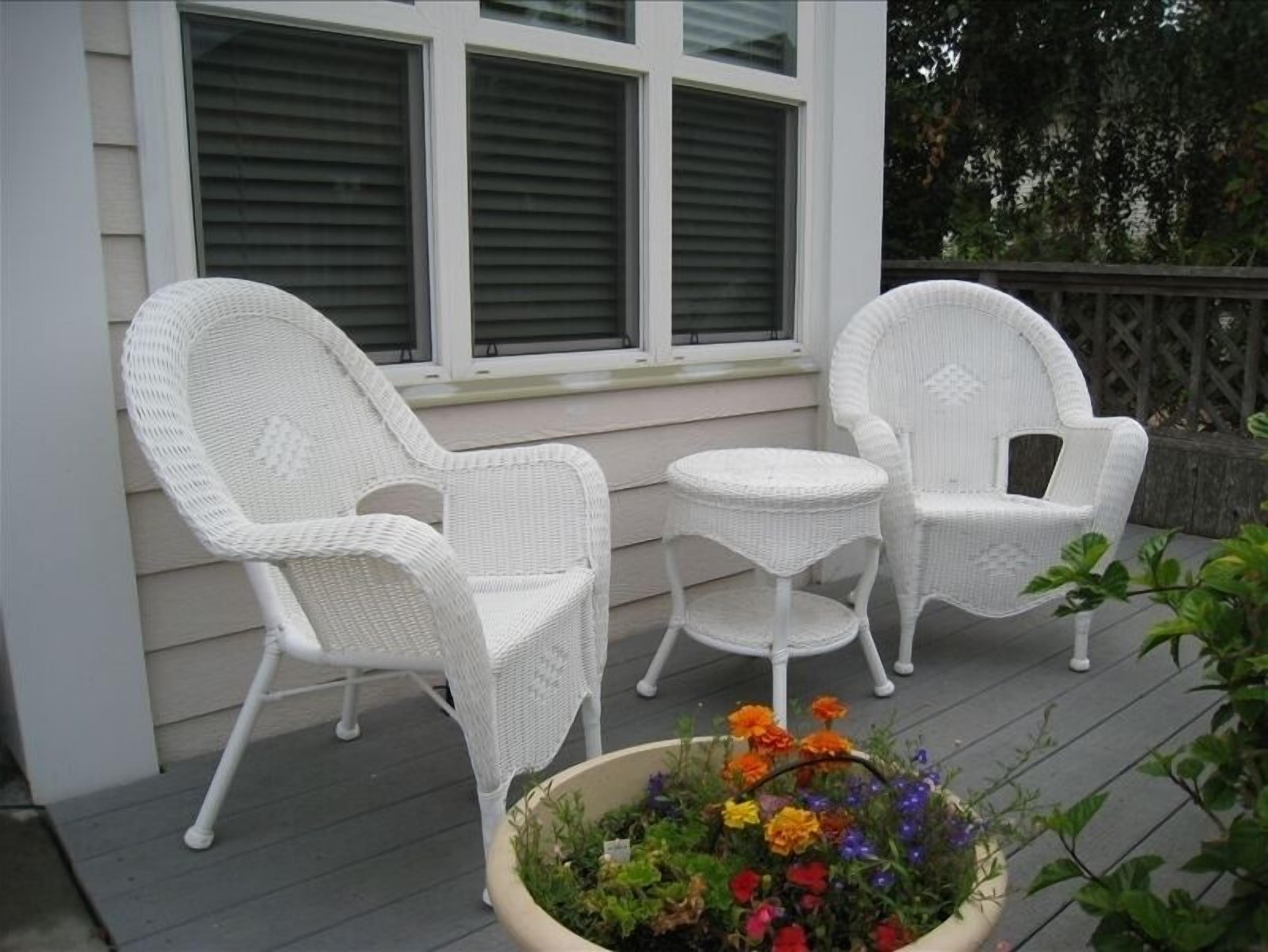 A porch with two white wicker chairs and a small round table.
