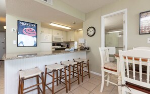 A kitchen with a bar area, a dining table with chairs, and a clock on the wall.