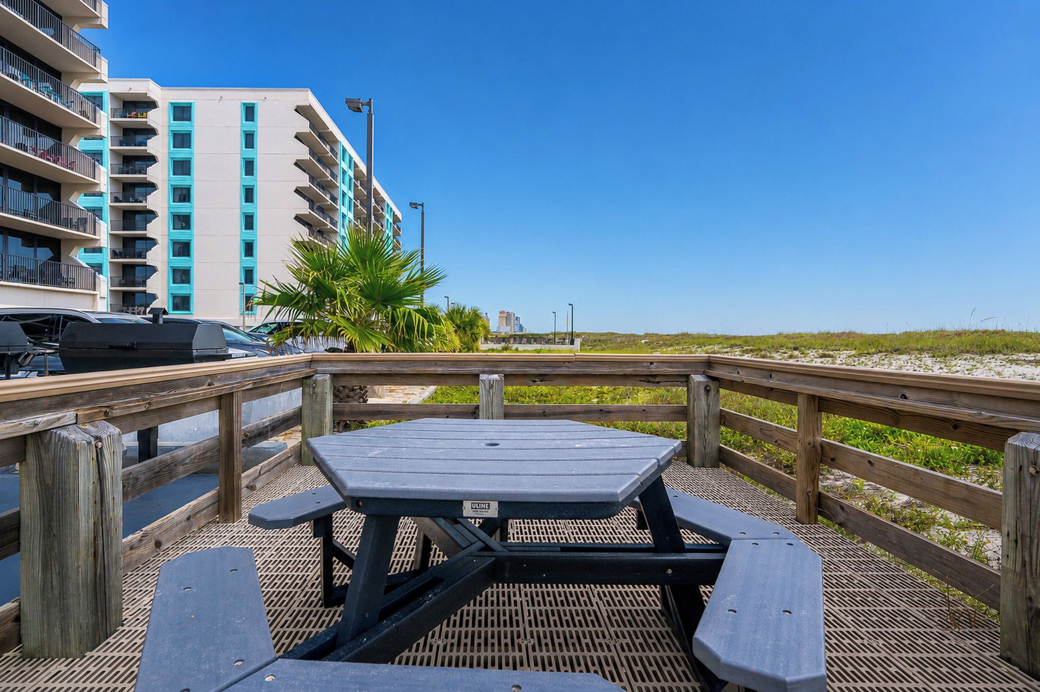 A wooden deck with picnic tables, a view of a building with balconies, and a clear sky.