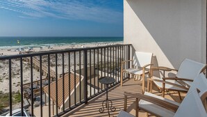 Un balcón con vista a la playa, sillas de madera y una pequeña mesa.
