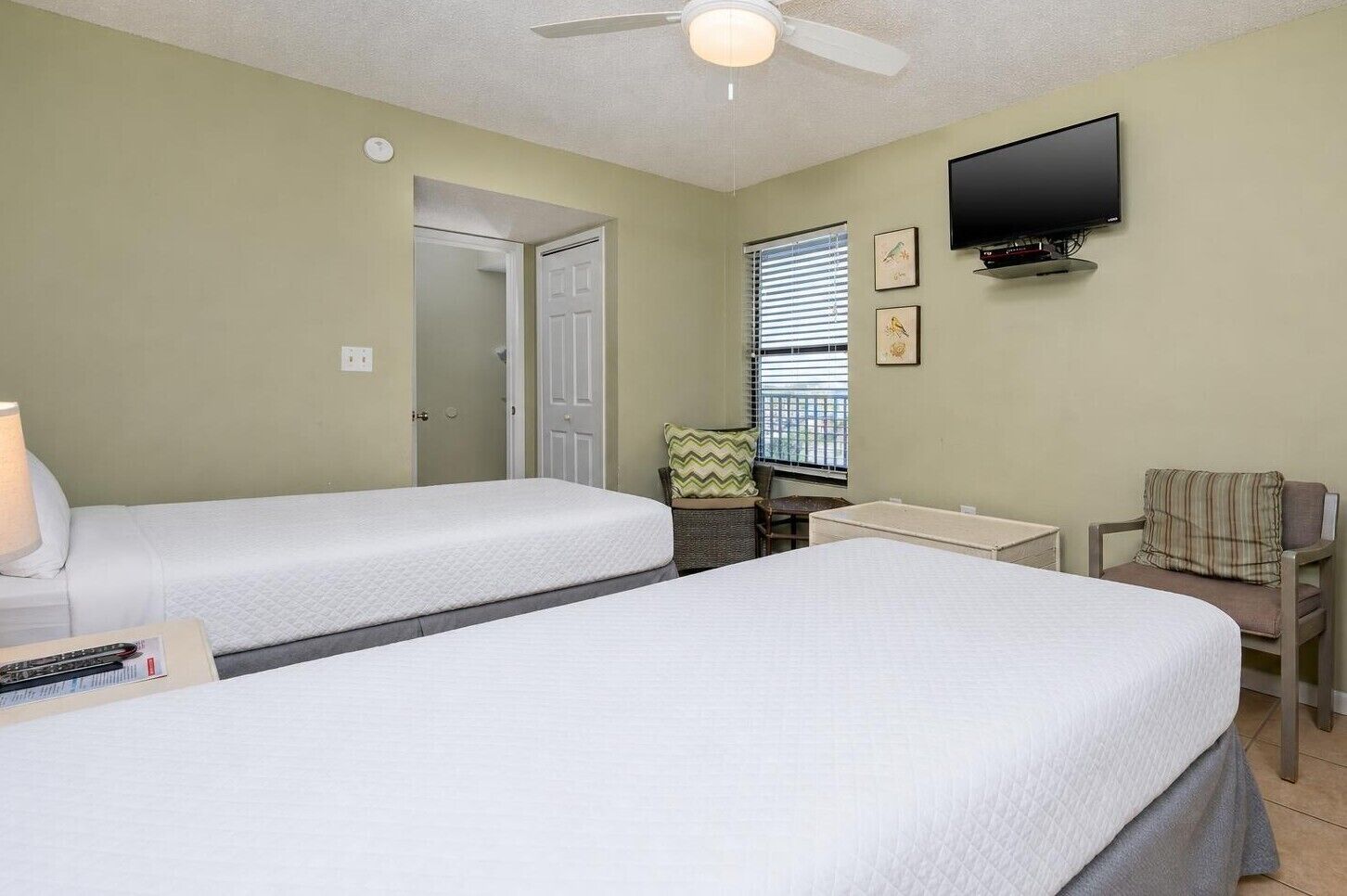 A hotel room with two beds, a desk, a chair, a television, and a window with blinds.